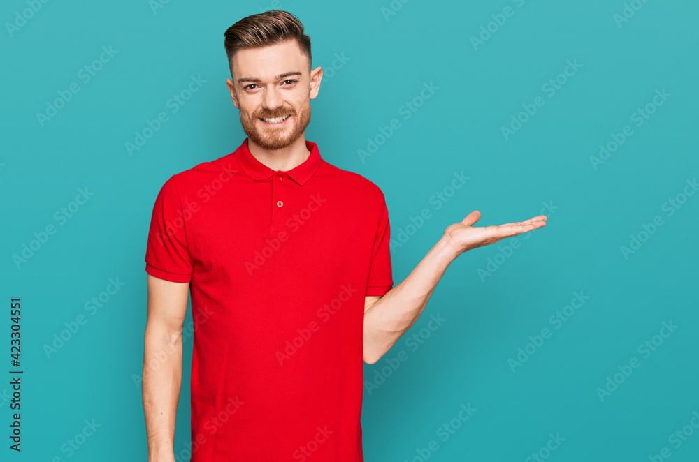 Young redhead man wearing casual clothes smiling cheerful presenting and pointing with palm of hand looking at the camera. Young redhead man wearing casual clothes smiling cheerful presenting and pointing with palm of hand looking at the camera.