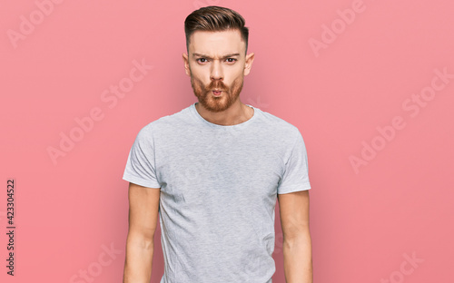Young redhead man wearing casual grey t shirt making fish face with lips, crazy and comical gesture. funny expression.