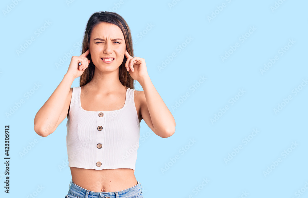Young beautiful girl wearing casual sleeveless t shirt covering ears with fingers with annoyed expression for the noise of loud music. deaf concept. Young beautiful girl wearing casual sleeveless t shirt covering ears with fingers with annoyed expression for the noise of loud music. deaf concept.