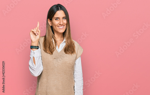 Young woman wearing casual clothes showing and pointing up with finger number one while smiling confident and happy.
