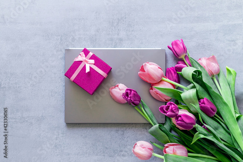 A gray laptop, a pink gift box, and a bouquet of tulips on a gray concrete background. Gift