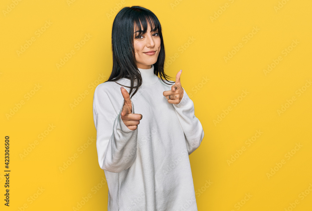 Young brunette woman with bangs wearing casual turtleneck sweater pointing fingers to camera with happy and funny face. good energy and vibes. Young brunette woman with bangs wearing casual turtleneck sweater pointing fingers to camera with happy and funny face. good energy and vibes.