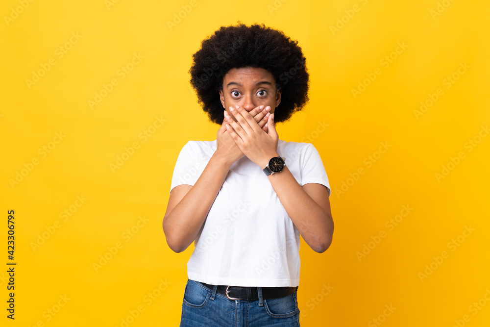 Young African American woman isolated on yellow background covering mouth with hands Young African American woman isolated on yellow background covering mouth with hands