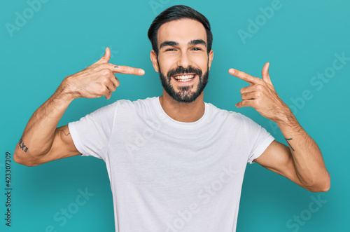 Young hispanic man wearing casual white t shirt smiling cheerful showing and pointing with fingers teeth and mouth. dental health concept.