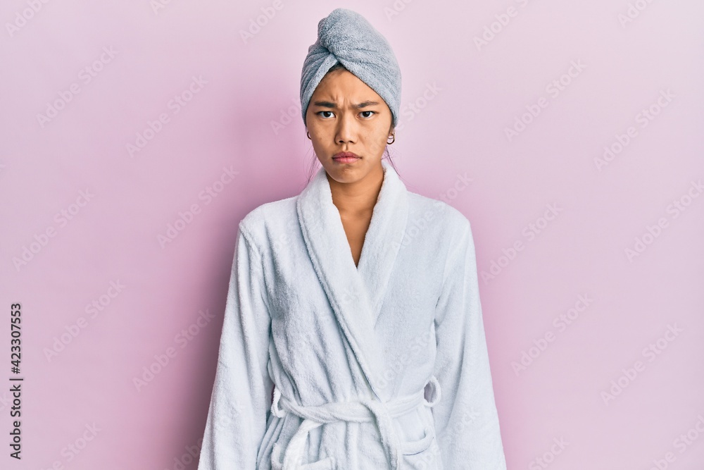 Young chinese woman wearing shower towel cap and bathrobe skeptic and nervous, frowning upset because of problem. negative person.