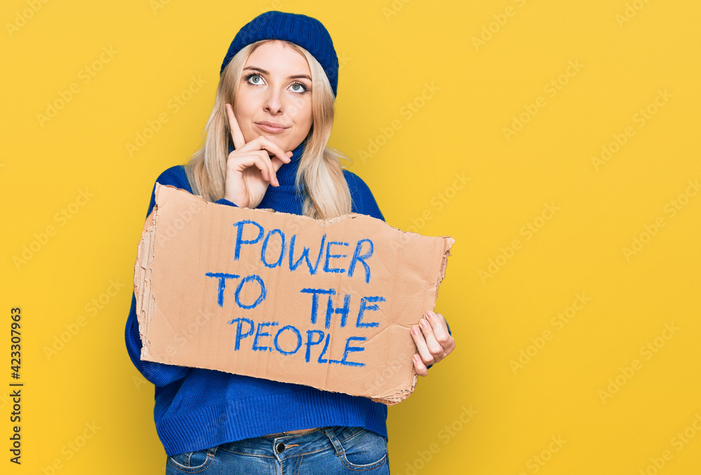 Young caucasian woman holding power to the people banner serious face thinking about question with hand on chin, thoughtful about confusing idea Young caucasian woman holding power to the people banner serious face thinking about question with hand on chin, thoughtful about confusing idea