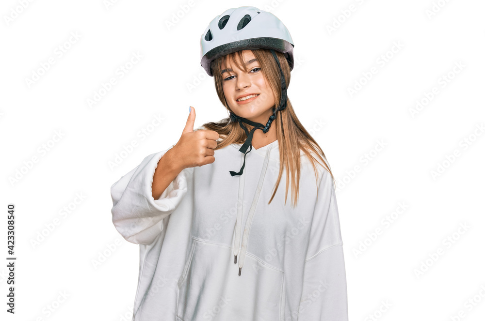 Teenager caucasian girl wearing bike helmet doing happy thumbs up gesture with hand. approving expression looking at the camera showing success. Teenager caucasian girl wearing bike helmet doing happy thumbs up gesture with hand. approving expression looking at the camera showing success.