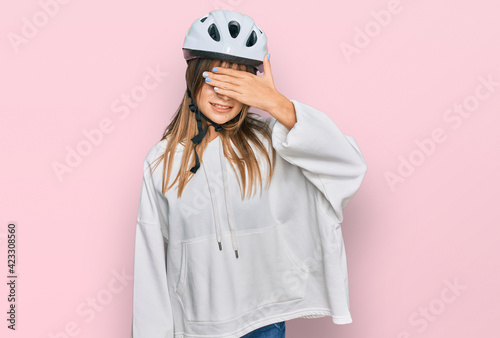 Teenager caucasian girl wearing bike helmet smiling and laughing with hand on face covering eyes for surprise. blind concept. © Krakenimages.com