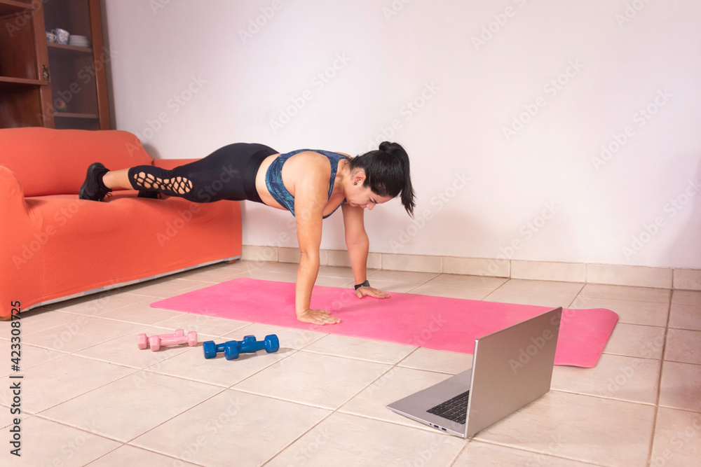 Young fit woman doing plank with feet on top of couch, in living room, exercising at home during quarantine. Young fit woman doing plank with feet on top of couch, in living room, exercising at home during quarantine.