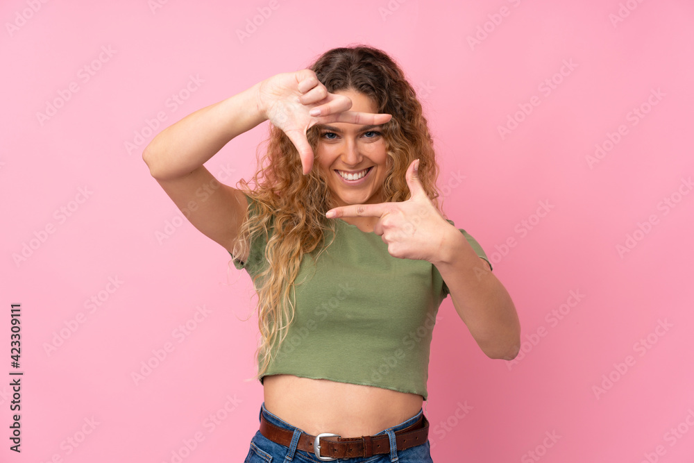 Young blonde woman with curly hair isolated on pink background focusing face. Framing symbol Young blonde woman with curly hair isolated on pink background focusing face. Framing symbol