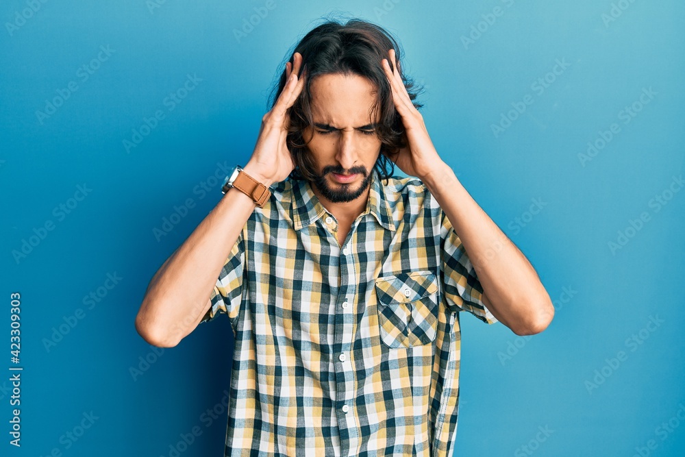 Young hispanic man wearing casual clothes with hand on head for pain in head because stress. suffering migraine. Young hispanic man wearing casual clothes with hand on head for pain in head because stress. suffering migraine.