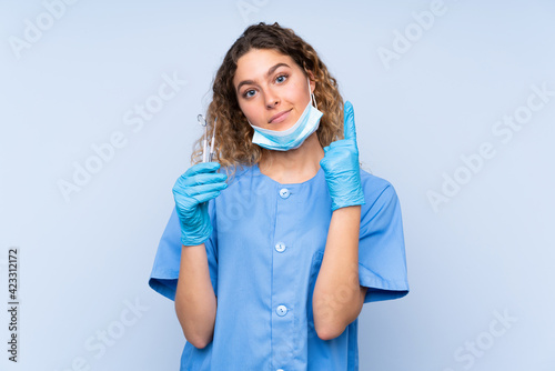 Young blonde woman dentist holding tools isolated on blue background pointing with the index finger a great idea