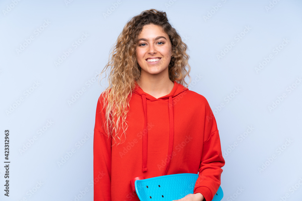 Obraz premium Young blonde woman with curly hair isolated on blue background with a skate