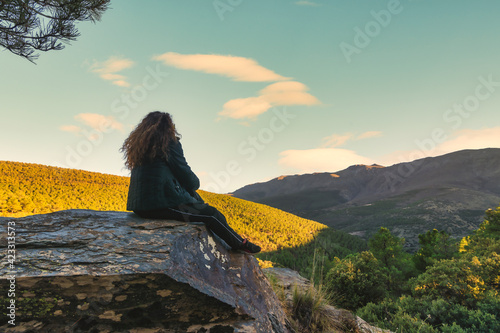 Long-haired woman sitting on a rock looking at the sky and mountains.