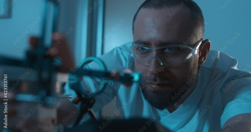 In the dark dental office on the desk is axiosplit device with the ceramic model of upper jaw inside and male medical worker with beard and disposable gloves taking to check an upper part. In the dark dental office on the desk is axiosplit device with the ceramic model of upper jaw inside and male medical worker with beard and disposable gloves taking to check an upper part.