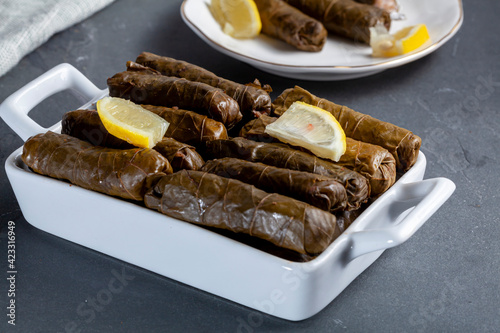 Yaprak sarmasi is a traditional Turkish dish made by wrapping rice stuffing with grape leaves.  A tray of hand rolled sarmas are served on stone background with slices of lemon for added flavor. photo