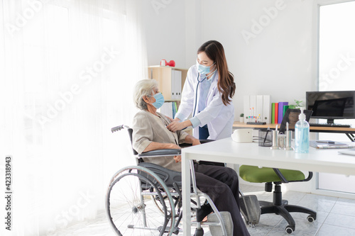 Asian doctor talk with old female patient about disease symptom  doctor use stethoscope listening lung of patient  elderly health check up   they wear surgical mask  corona virus 