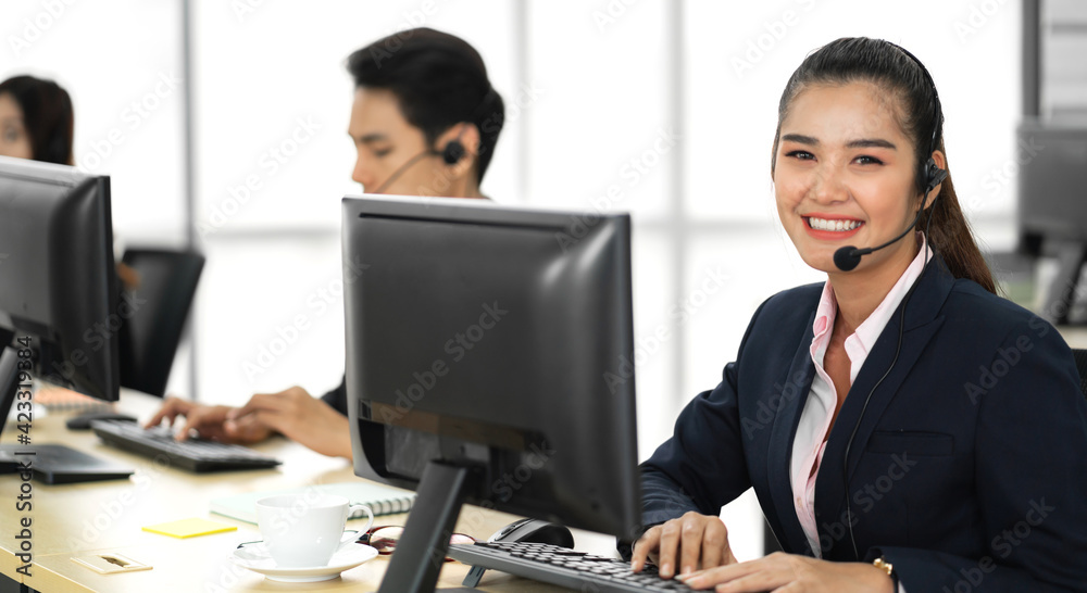 Group of happy asian smiling call center business operator customer help support team phone services agen working and talking with headset on desktop computer at call center office Group of happy asian smiling call center business operator customer help support team phone services agen working and talking with headset on desktop computer at call center office