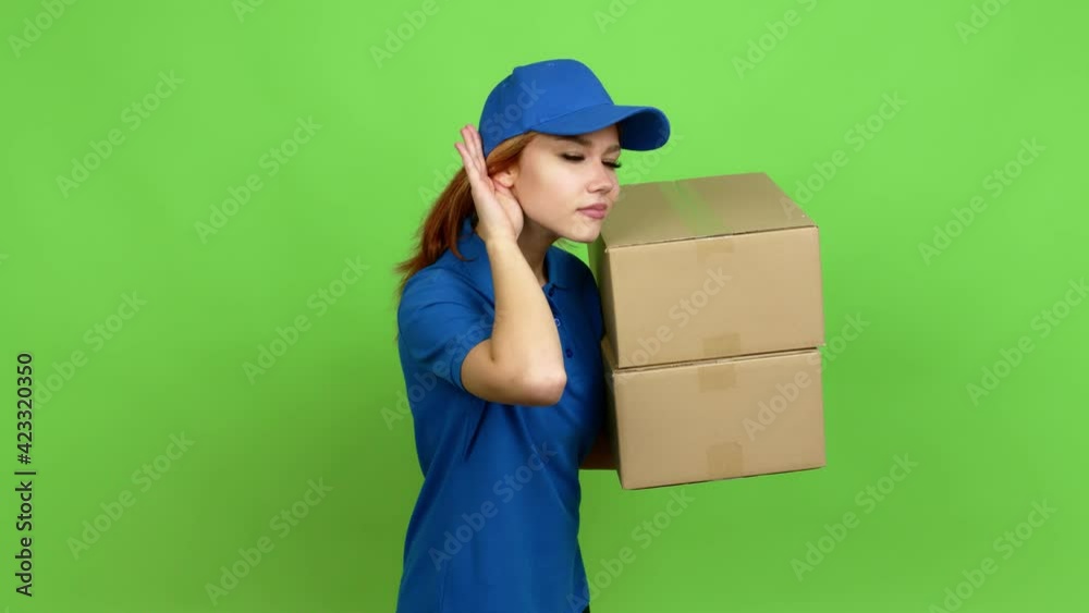 Young blonde teenager girl holding boxes for delivery listening something over isolated background. Green screen chroma key