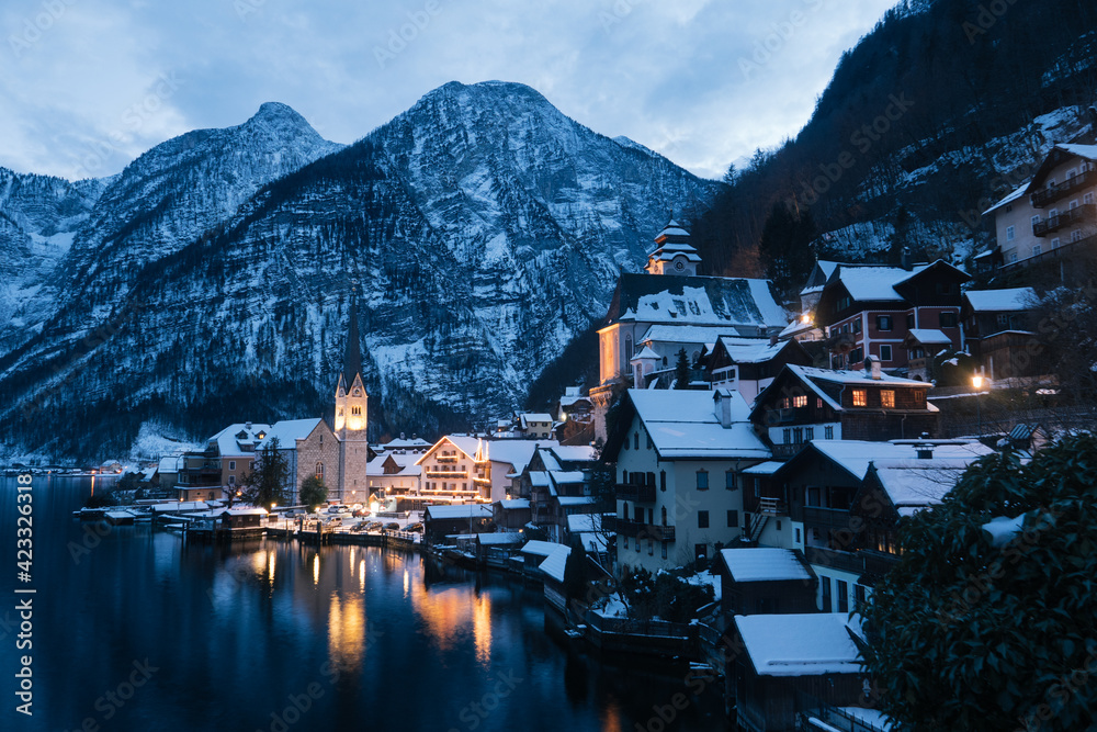 Hallstatt Cityscape on a Cold Winter Evening Covered with Snow with the Lake Hallstaetter See and Church Illuminated at Night