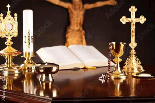Religious holiday – Easter. Catholic symbols composition. Jesus figure, The Cross, monstrance, Holy Bible, rosary and golden chalice on gray background. 