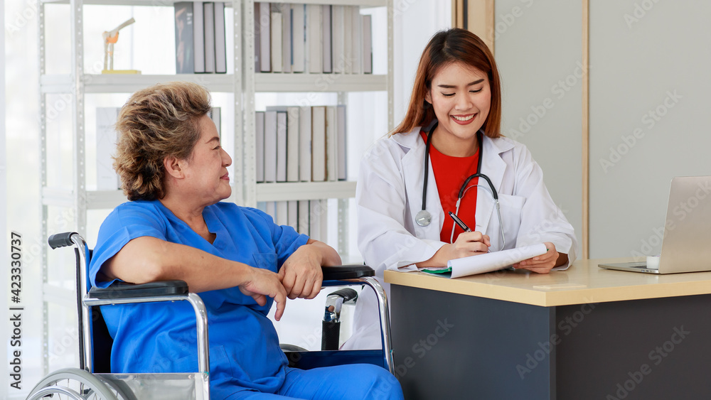 Obraz premium Asian woman doctor writing note and near with elderly female as sitting on wheelchair both of them are smiling look to happy and comfortable at hospital in the morning