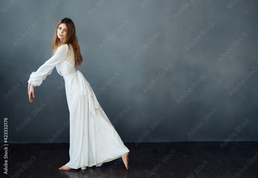 Beautiful woman in a white dress to the floor on a gray background in full growth Beautiful woman in a white dress to the floor on a gray background in full growth