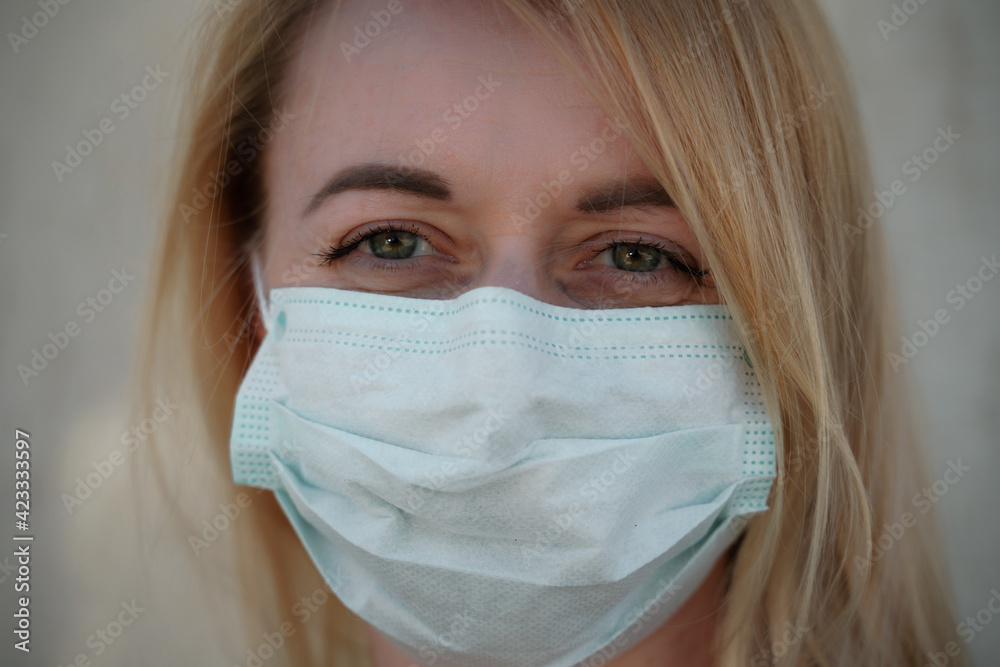 Close-up portrait of a young blonde woman in a medical mask on a light background. Virus protection. Coronovirus covid-19 The concept of a pandemic epidemic. Quarantine. Stay at home. Close-up portrait of a young blonde woman in a medical mask on a light background. Virus protection. Coronovirus covid-19 The concept of a pandemic epidemic. Quarantine. Stay at home.