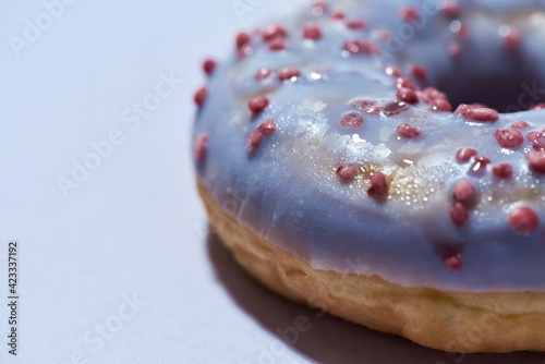 Close up shot of a freshly baked delicious donut with sprinkles and sugar glaze isolated on purple background