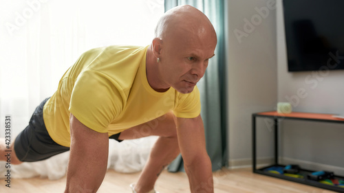 Portrait of bald man, fitness coach stretching his body, working out in living room at home on a daytime
