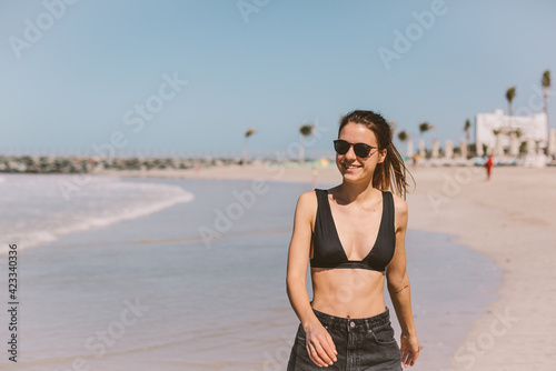 Young lovely girl in shorts and sunglasses running on beach. 