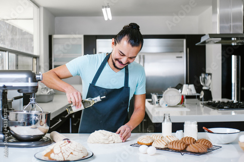 portrait of Latin man standing in kitchen baking and holding Conchas traditional Mexican bread in Mexico city