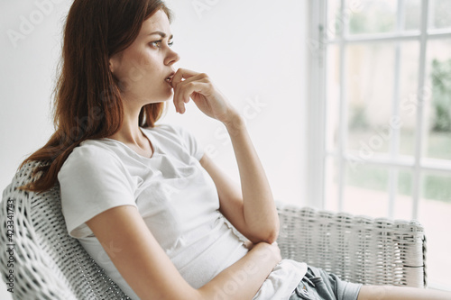 Bild auf Leinwand perplexed woman in white t-shirt sits in a chair and looks out the window
