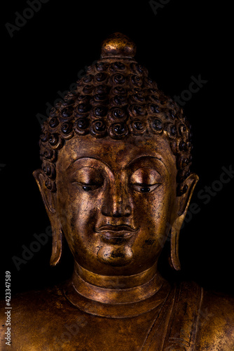 Portrait image close up of ancient art Buddhist statue isolated front side on isolated black background.