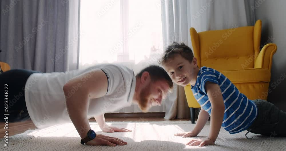 Dad and little son do sports, float at home by the sun window.