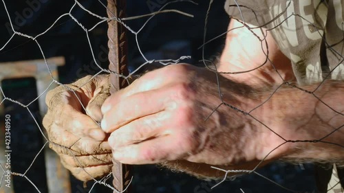 Close-up of a farmer's hands fixing a fence in a field. Concept of maintenance work in the field.