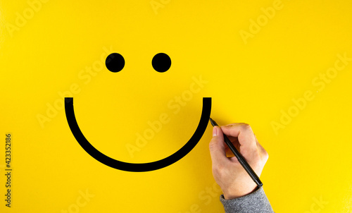 Male hand drawing a smiling happy face sketch on yellow background. Client satisfaction.
