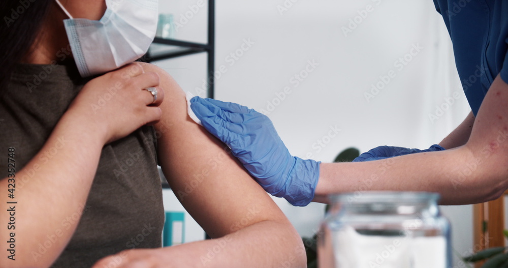 Close-up nurse in blue scrubs, medical gloves gives vaccine injection shot with hypodermic needle to young female client