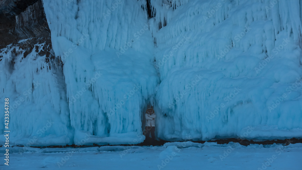 The rock is covered with a thick layer of bizarre ice splashes and icicles. In a small grotto at the base, there is a man in a down jacket and a hood. He folded his arms over his chest. Coldly. Baikal