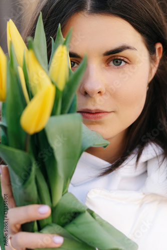 Portrait of a girl with yellow tulips. Girl in a white jacket.