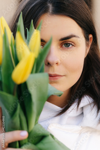 Portrait of a girl with yellow tulips. Girl in a white jacket.