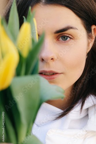 Portrait of a girl with yellow tulips. Girl in a white jacket.