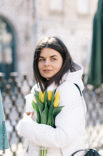 Portrait of a girl with yellow tulips. Girl in a white jacket.