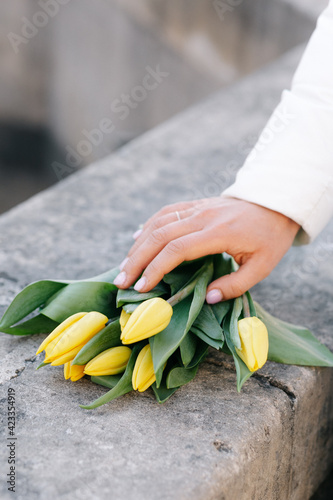 The girl holds her hand on a bouquet of yellow tulips that lie on the stone surface.