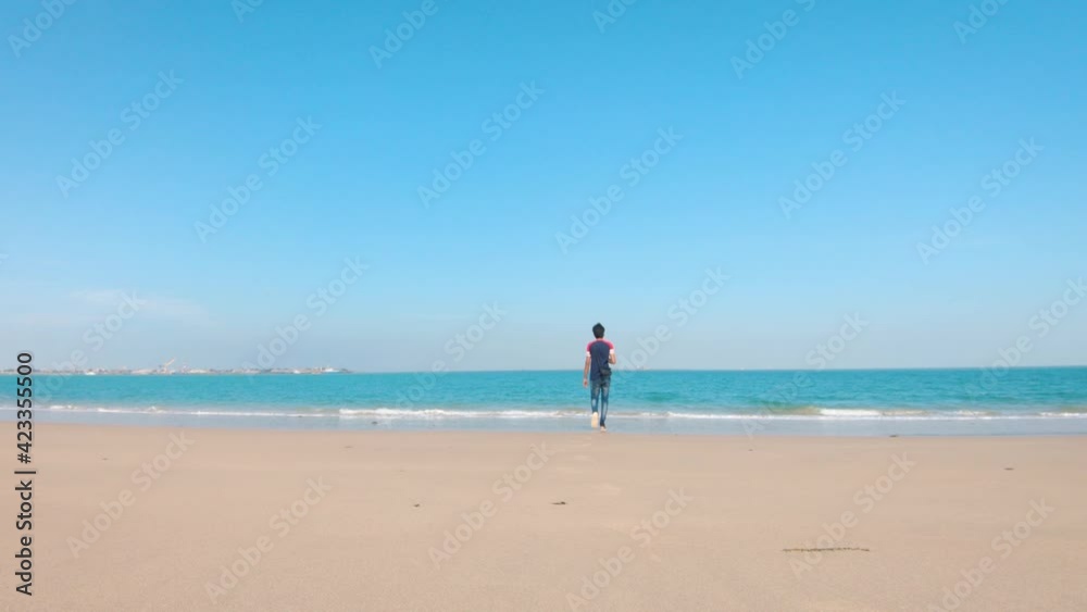 Young Indian man walking on the beach towards sea in summer at Bet Dwarka in Gujarat, India. Summer Relaxation beach background Young Indian man walking on the beach towards sea in summer at Bet Dwarka in Gujarat, India. Summer Relaxation beach background