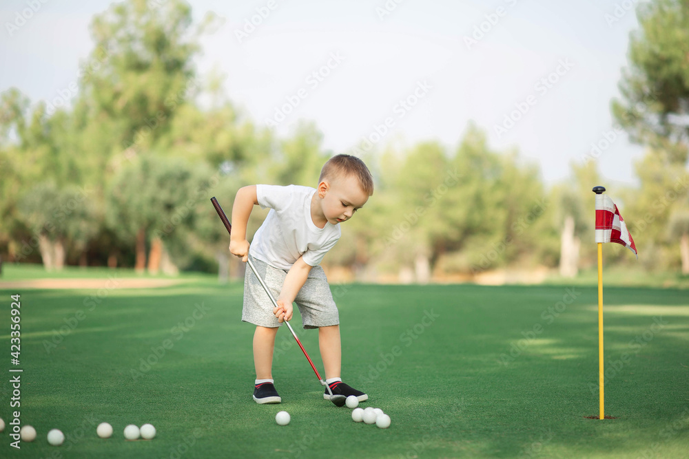 little Boy playing golf and hitting ball by putter on green grass