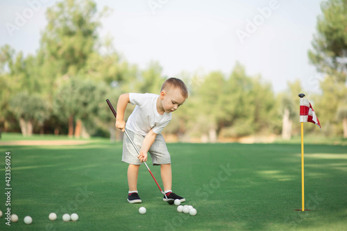 little Boy playing golf and hitting ball by putter on green grass
