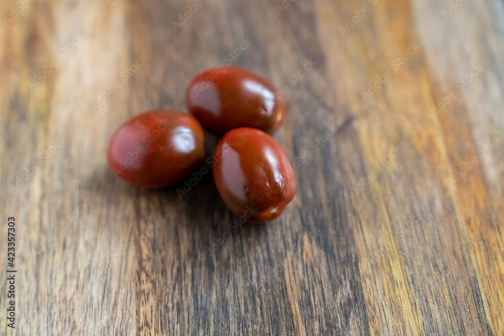 Obraz premium three black kumato cherry tomatoes on a wooden background vertically