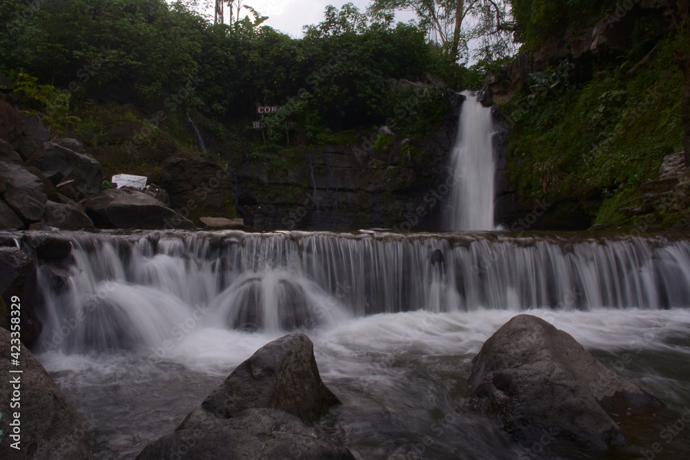 A stunning jungle waterfall flows into a cool mountain river with big rocks. A stunning jungle waterfall flows into a cool mountain river with big rocks.