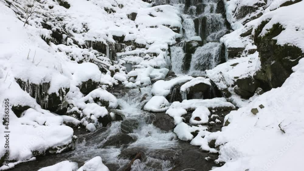 Small mountain streams of icy water flow among wet stones covered with white snow, 3X slow-motion Small mountain streams of icy water flow among wet stones covered with white snow, 3X slow-motion